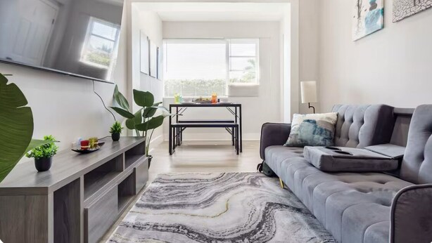 Una sala de estar moderna con un sofá gris, un televisor de pantalla plana montado en la pared, una mesa de centro y una planta grande.