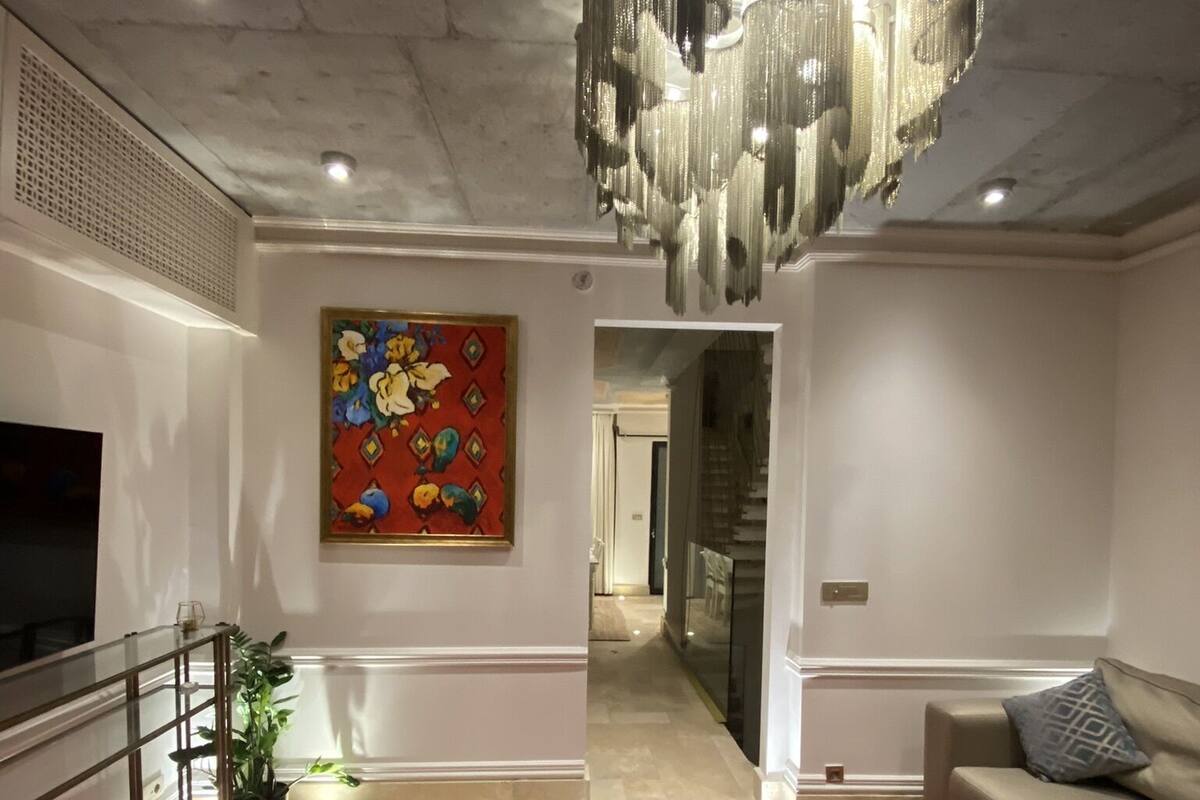 Un salon avec une moquette rouge, une table basse en verre, un canapé, un téléviseur et un tableau coloré accroché au mur.