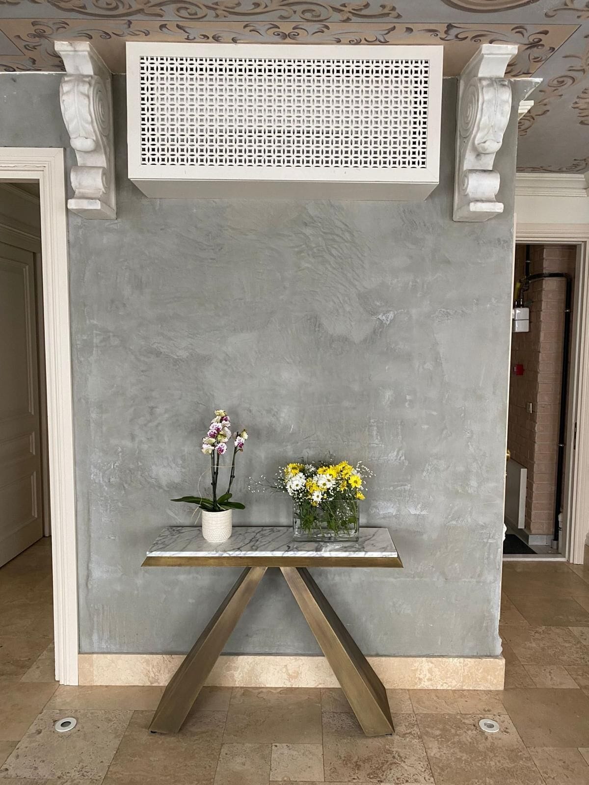 Un comptoir d’accueil en marbre agrémenté de deux vases de fleurs, une grille décorative au plafond et un sol en marbre.
