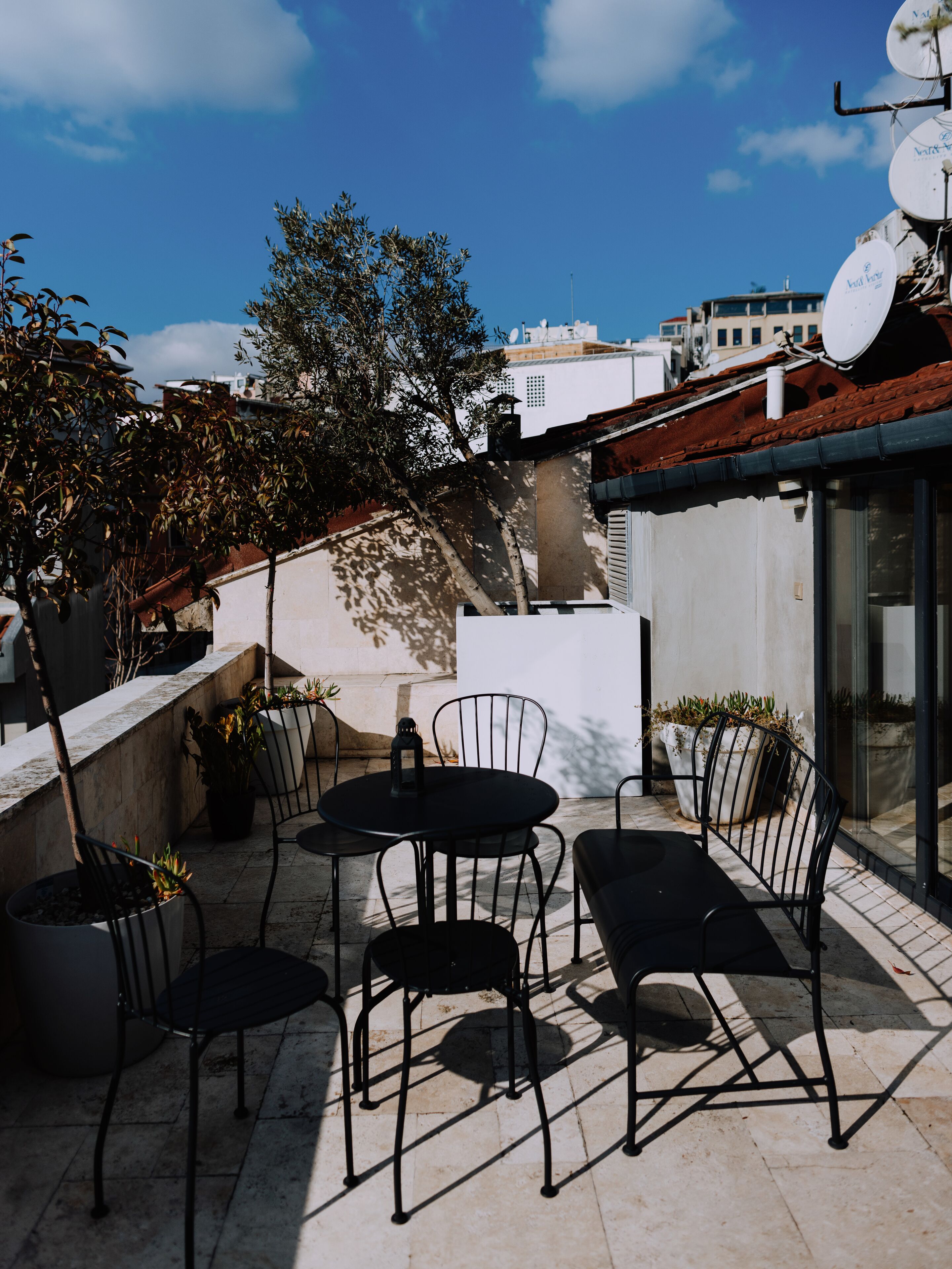 Terrassa al terrat amb taula i cadires, plantes en testos i vista a edificis al fons.