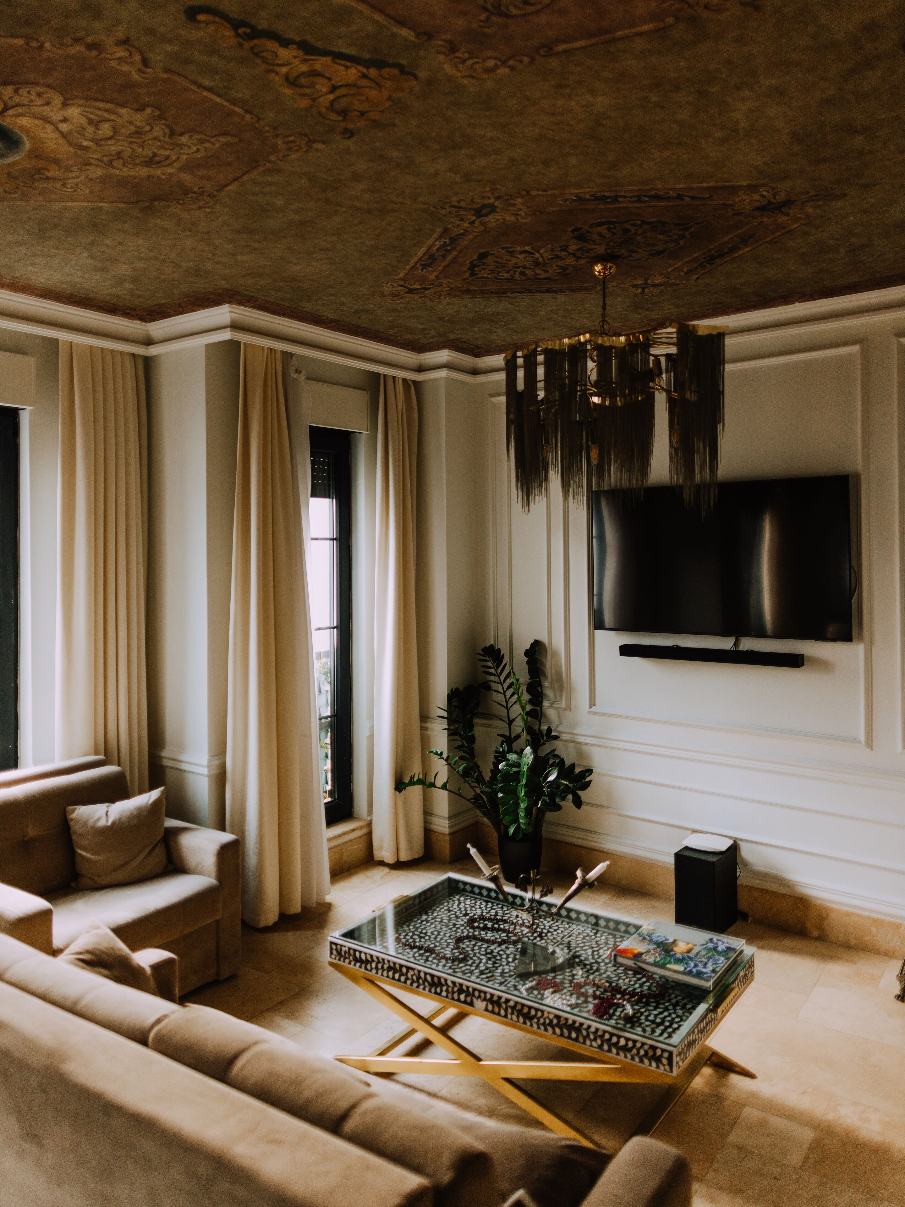Een ruime woonkamer met een beige bank, een glazen salontafel en een grote flatscreen televisie aan de muur.