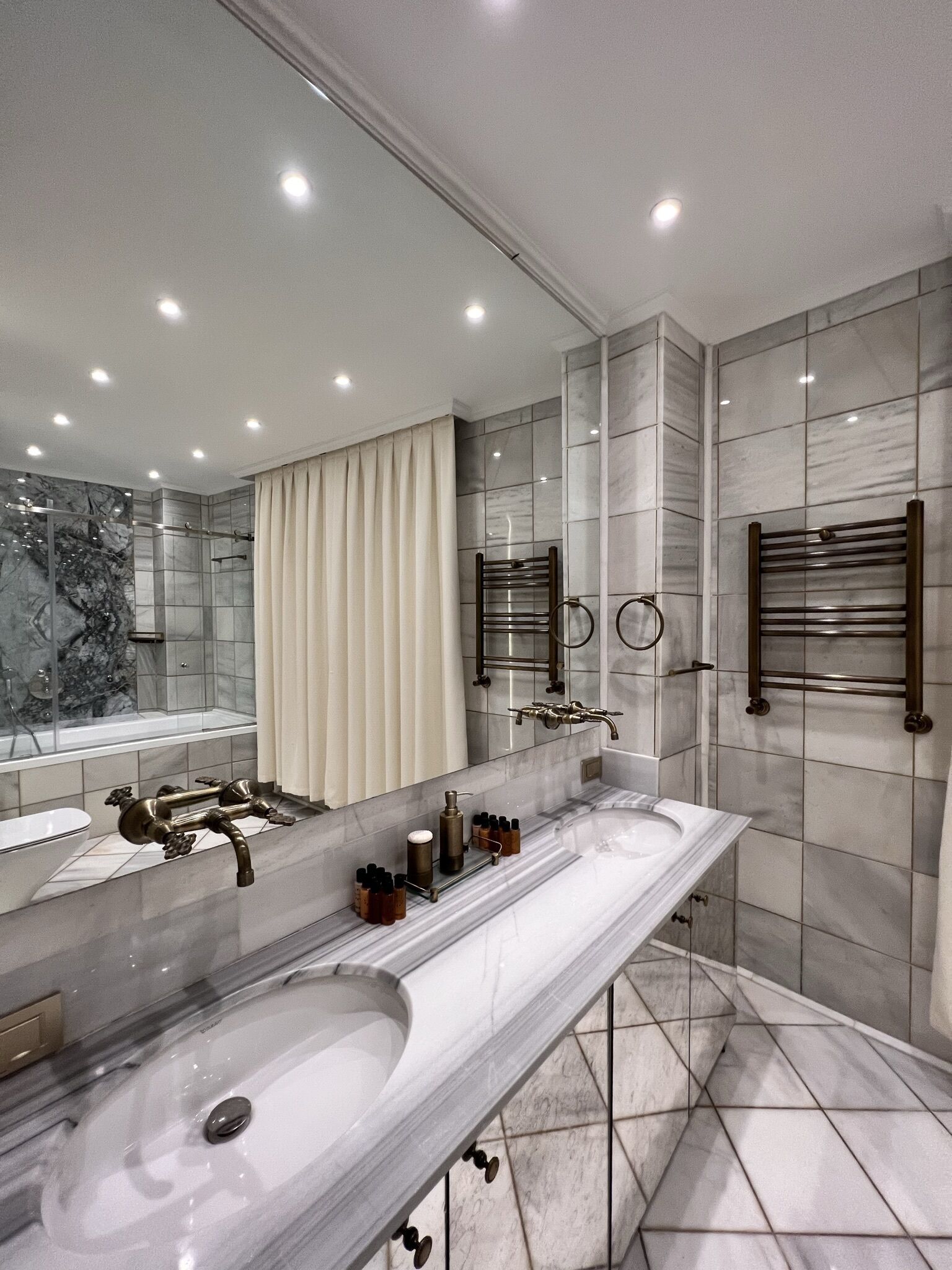 A modern bathroom with a large vanity, dual sinks, a glass shower enclosure, and marble tiles.