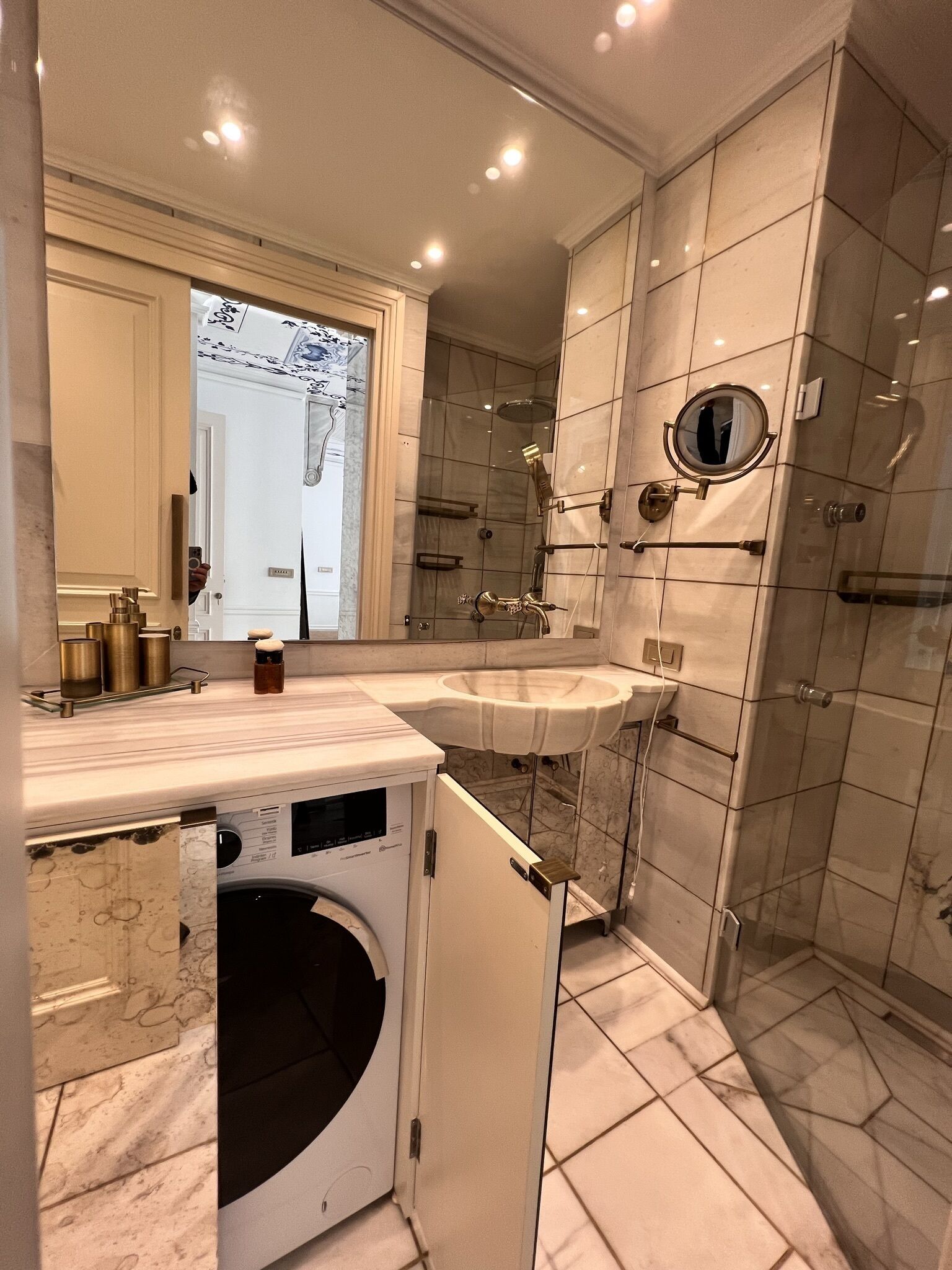 A modern bathroom with a large mirror, a sink, a shower, and a built-in washing machine.