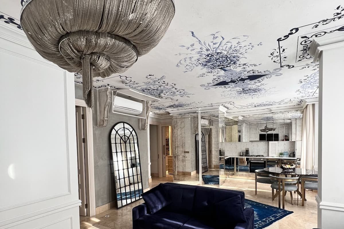 Un salon spacieux avec un grand canapé bleu, une table basse ronde et un luminaire décoratif au plafond.