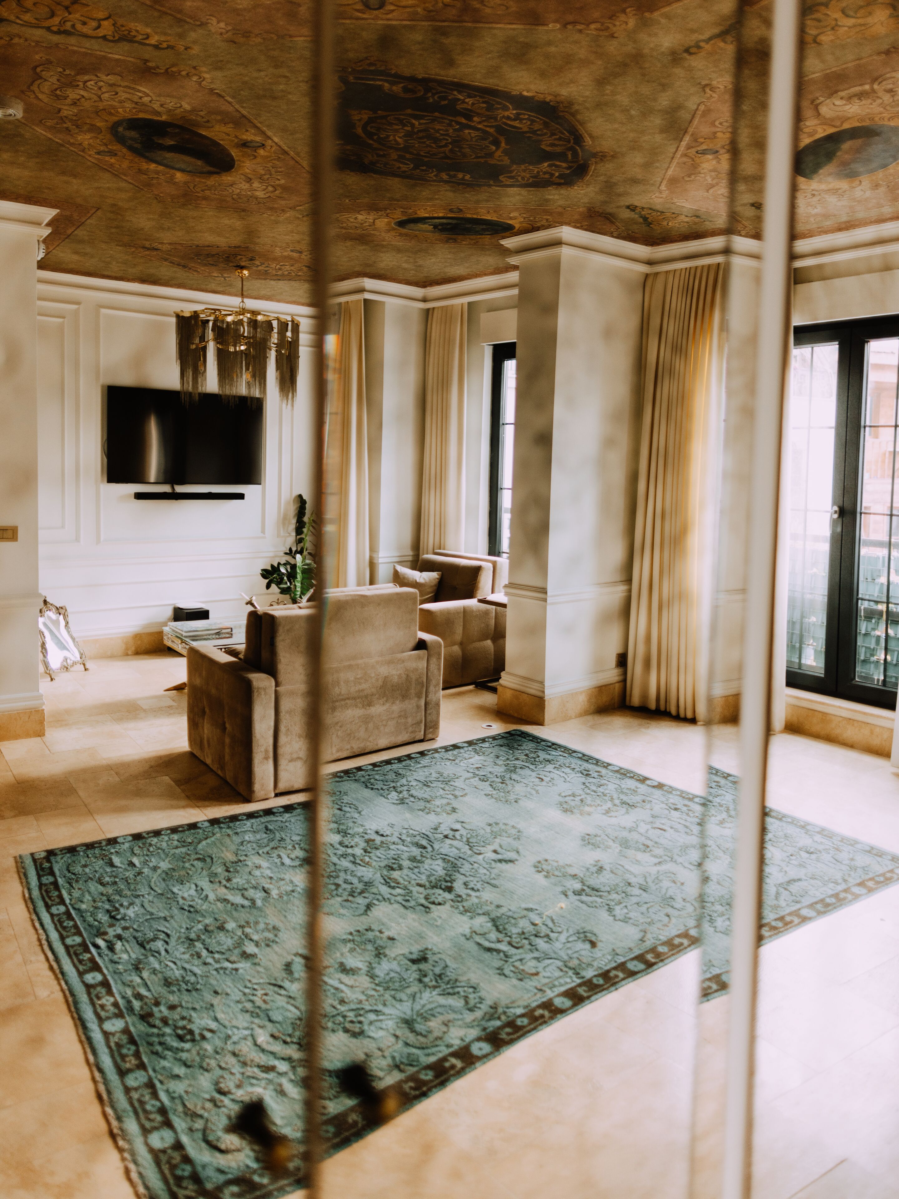 Un vaste salon agrémenté d’un grand tapis à motifs verts, d’un téléviseur à écran plat fixé au mur et d’un coin salon confortable composé de deux fauteuils et d’un canapé.