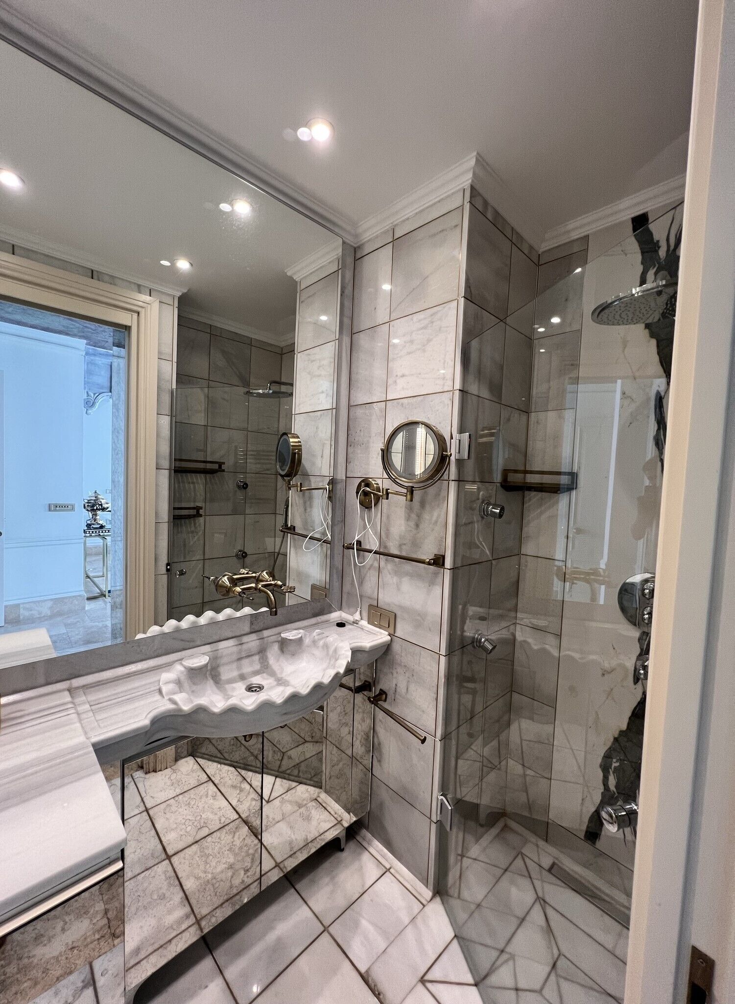 Un baño moderno con lavamanos de mármol, cabina de ducha de vidrio y un espejo grande.