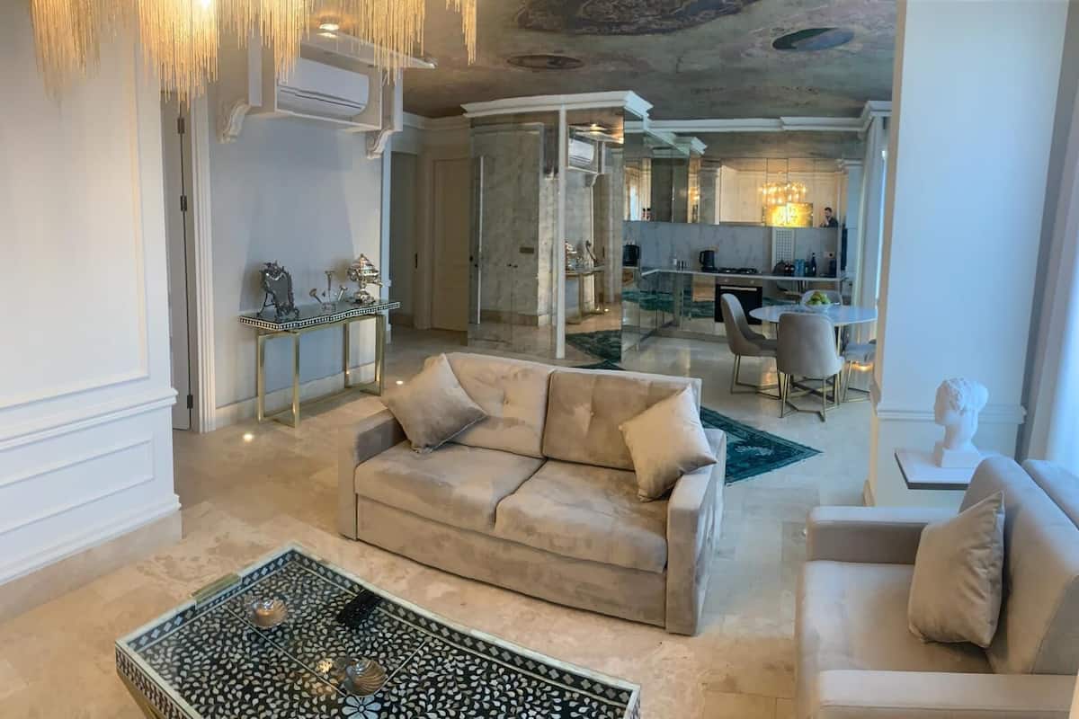 Un vaste espace de vie avec un canapé beige, une table basse et, au fond, un coin repas.