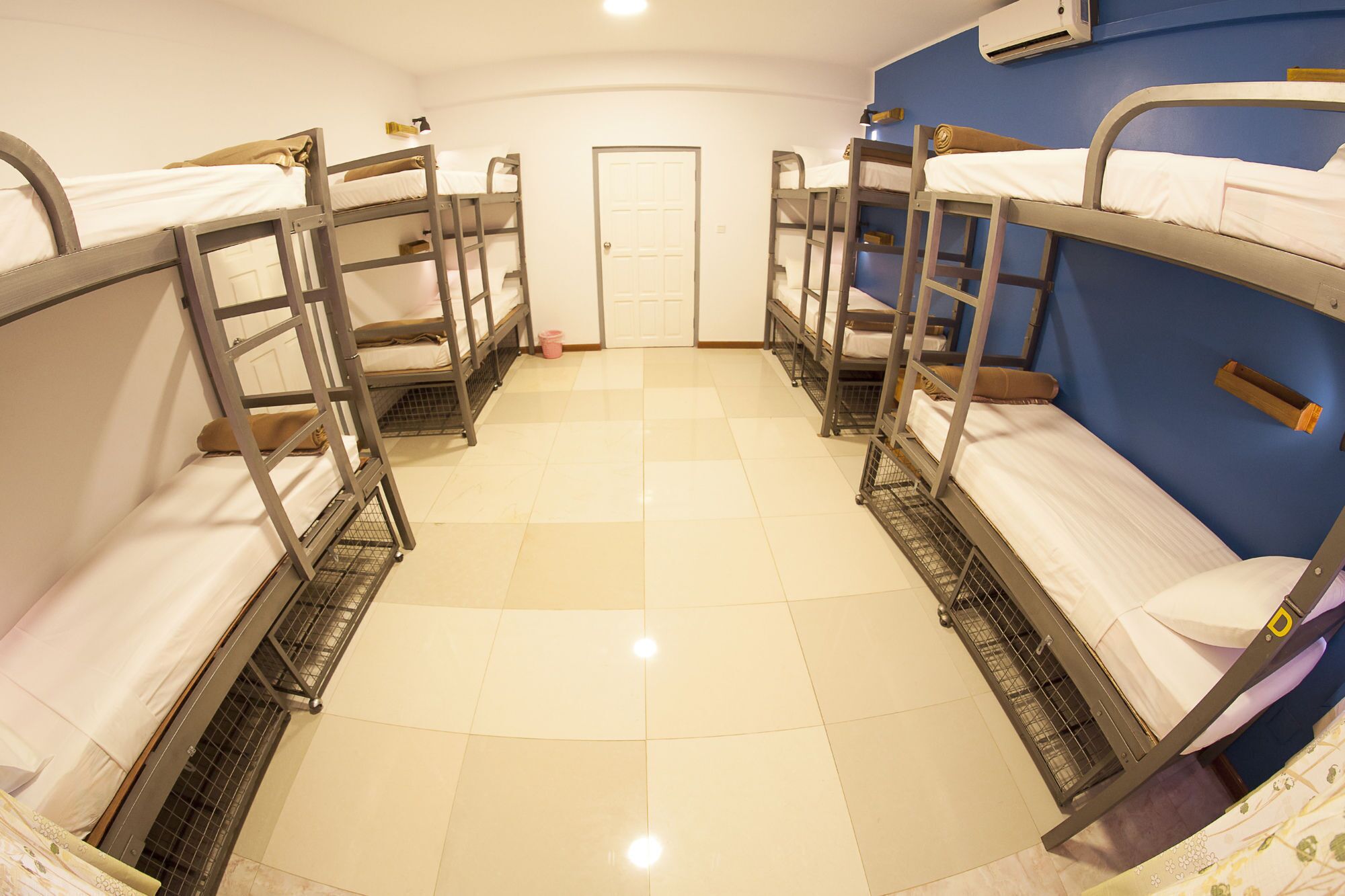 Une chambre de dortoir avec des lits superposés disposés en deux rangées, une porte et un sol carrelé.