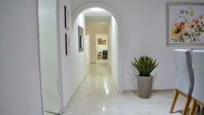 Een hal met betegelde vloer, een potplant en een eetgedeelte met stoelen.