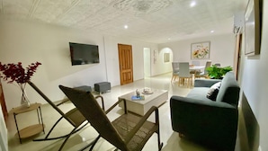Een moderne woonkamer met een bank, een salontafel en een aan de muur bevestigde televisie.