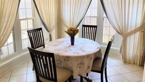 A dining area with a round table covered by a floral tablecloth, surrounded by four wooden chairs. - Sprawling Ranch Home (Fort Worth)
