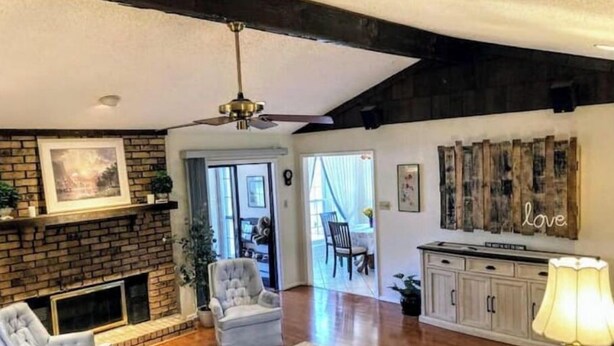 A living room with a fireplace, a ceiling fan, a dining area with a table and chairs, and a kitchen area with cabinets and a TV. - Sprawling Ranch Home (Fort Worth)