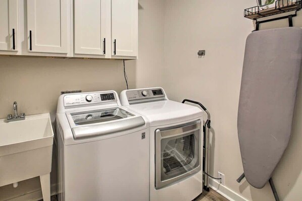 A compact laundry area with a washing machine, dryer, and ironing board.