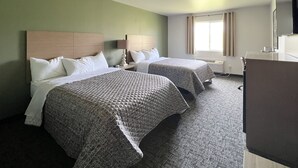 Une chambre d’hôtel avec deux lits, un bureau, une chaise, une lampe et une fenêtre avec des rideaux.