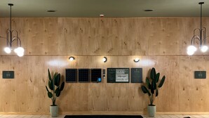 Un hall d'accueil d'hôtel avec un lambris en bois, un comptoir de réception noir, trois panneaux d'information, des plantes en pot et un tapis noir.