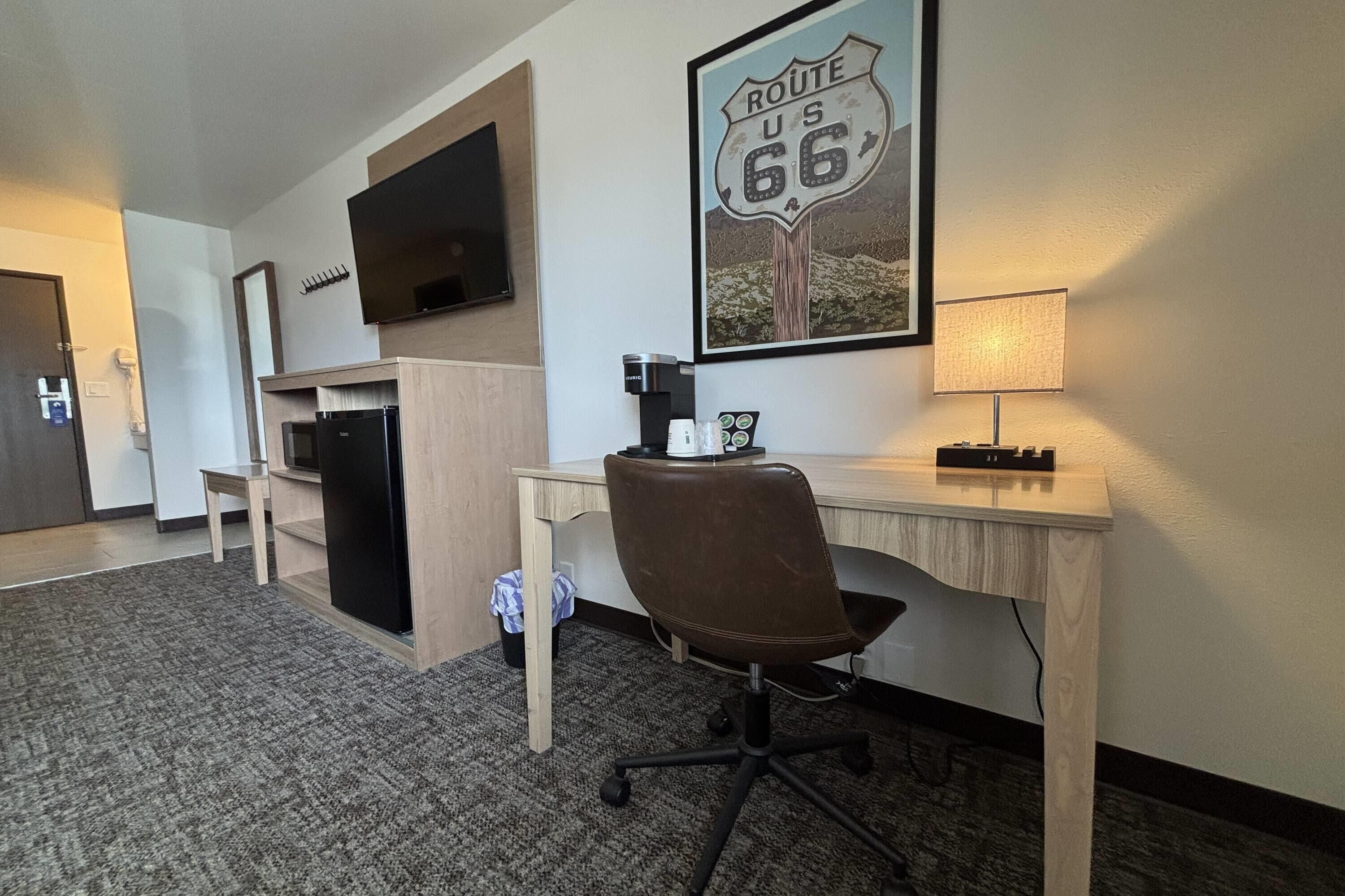 A hotel room with a desk, chair, television, coffee maker, and a Route 66 poster.