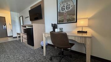 A hotel room with a desk, chair, television, coffee maker, and a Route 66 poster.