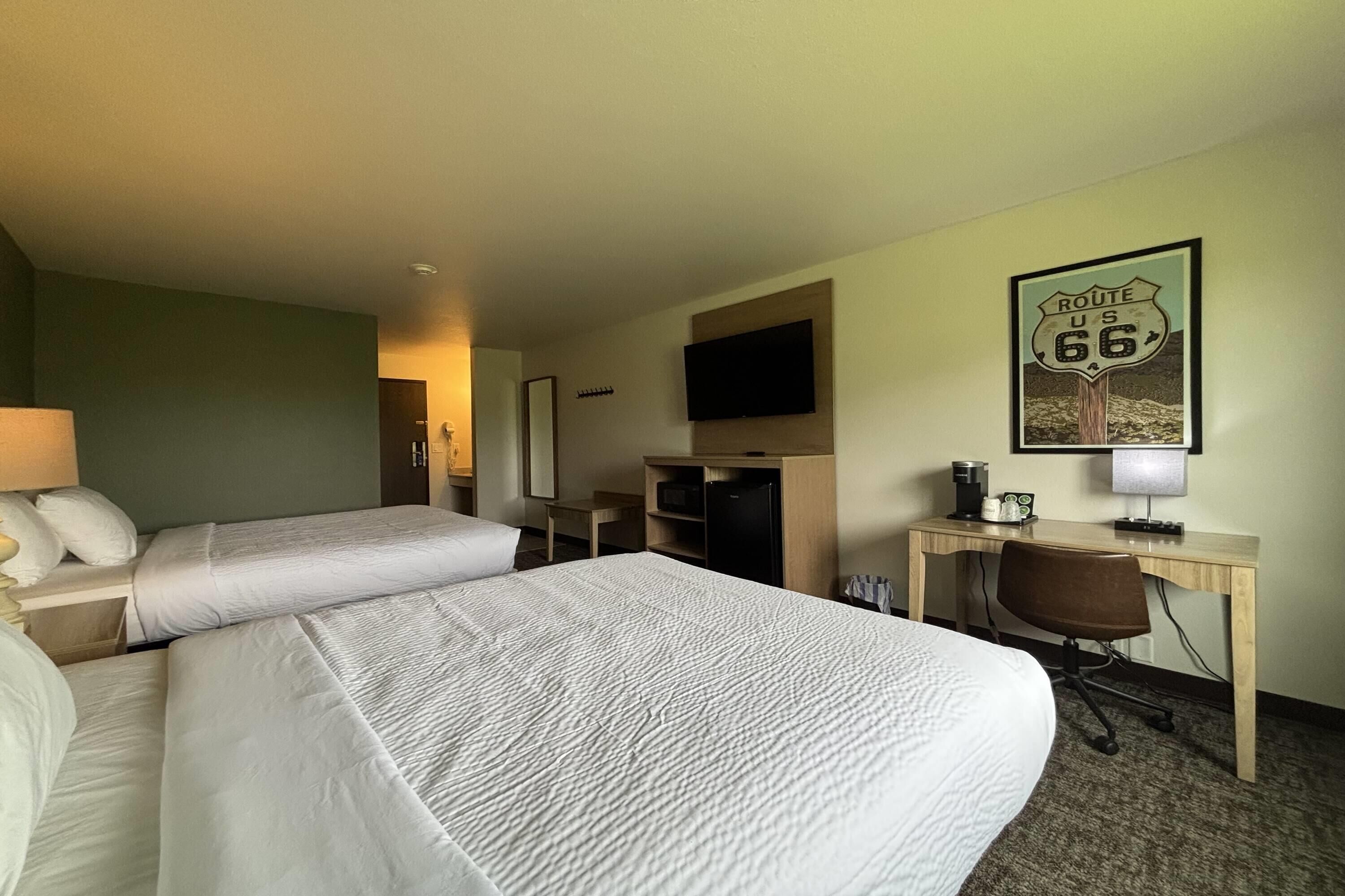 Une chambre d’hôtel avec deux lits, un bureau avec une chaise, une télévision, une machine à café et un panneau indiquant la Route 66.