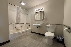 A bathroom with a bathtub, toilet, sink, and a mirror with lights.