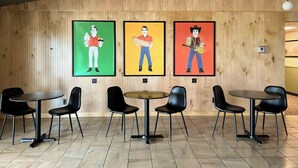 L’intérieur d’un restaurant présente des murs lambrés, trois œuvres d’art encadrées représentant des hommes portant des tenues différentes, ainsi que des chaises et des tables noires disposées pour accueillir les clients.