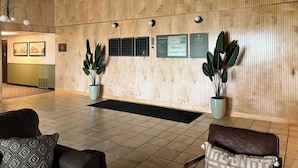 Un espace d’accueil avec un mur en bois, des plantes en pot, un comptoir d’accueil noir et un coin salon avec des chaises.