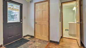 A hallway with a dark door, a wooden door, and a bathroom visible through an open door. - Alaskan Retreat Near Matanuska Glacier & River! (Sutton-Alpine)
