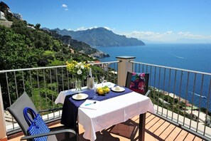 A balcony with a table set for two, overlooking a coastal landscape with mountains and the sea. - Amalfi Blu Retreat  (Amalfi)