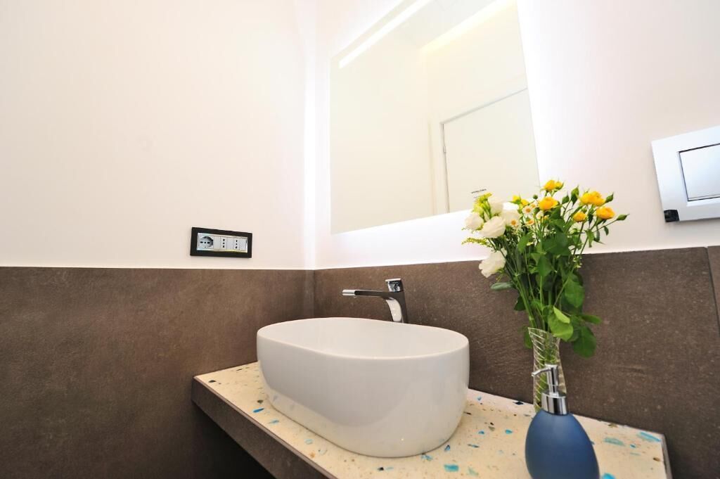 A bathroom with a white sink, a mirror, and a vase with flowers.