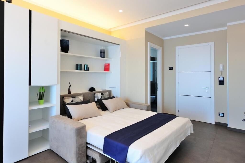A modern bedroom with a bed, built-in shelving, a wardrobe, and a door.