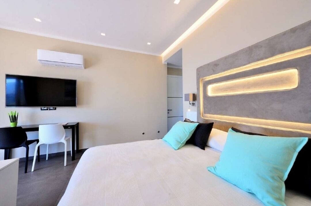 Une chambre d’hôtel moderne dotée d’un grand lit, d’un bureau avec une chaise, d’un téléviseur à écran plat fixé au mur et d’un panneau lumineux intégré au-dessus du lit.