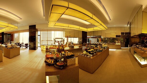 A spacious hotel lobby with a central buffet area, large windows, and a modern architectural design. - Grand Metropark Hotel Kunshan (Suzhou)