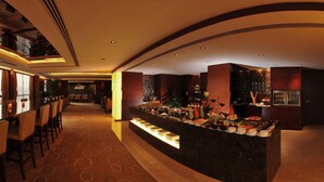 A hotel lobby with a long reception desk, a bar area with various food and drink items, and a seating area with tables and chairs. - Grand Metropark Hotel Kunshan (Suzhou)