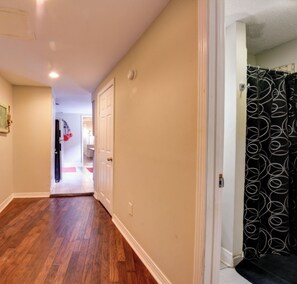 A hallway with wooden flooring, white walls, and a door leading to a bathroom with a black and white patterned shower curtain. - Steps to the French Quarter and Frenchman St spacious @1000sf Marigny (New Orleans)