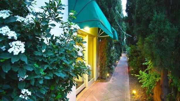 A pathway leading to a building with a green awning, surrounded by lush greenery and white flowers. - Soya Apartment Hotel (Melbourne)