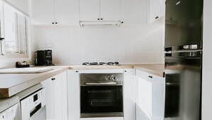 A modern kitchen with white cabinetry, a built-in oven, a coffee maker, and a stainless steel refrigerator. - Soya Apartment Hotel (Melbourne)