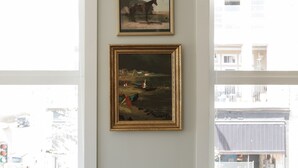 A room with a green sofa, a small table with a plant, and two framed paintings on the wall.