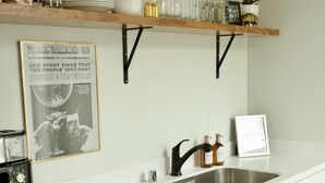 A kitchen with white cabinets, a stainless steel dishwasher, a double sink, and a wooden shelf above the counter.