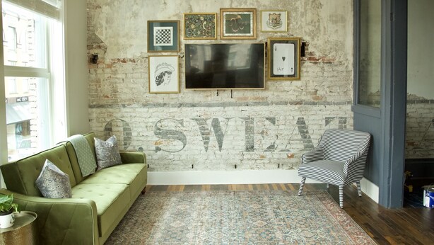 A room with a green sofa, a patterned rug, and a brick wall with framed artwork.