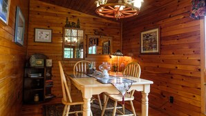 L’intérieur d’un chalet en bois comprend une table à manger, des chaises, un lustre et des tableaux encadrés accrochés aux murs.