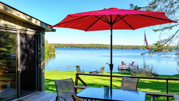 Une terrasse avec une table et des chaises, un parasol rouge et une vue sur un lac.