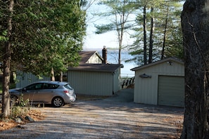 A gravel driveway leading to a wooden cabin with a chimney, a garage, and a car parked nearby.