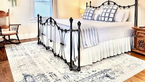 Une chambre à coucher avec un lit à baldaquin, une chaise en bois, une table de chevet, une lampe et une fenêtre avec des stores.