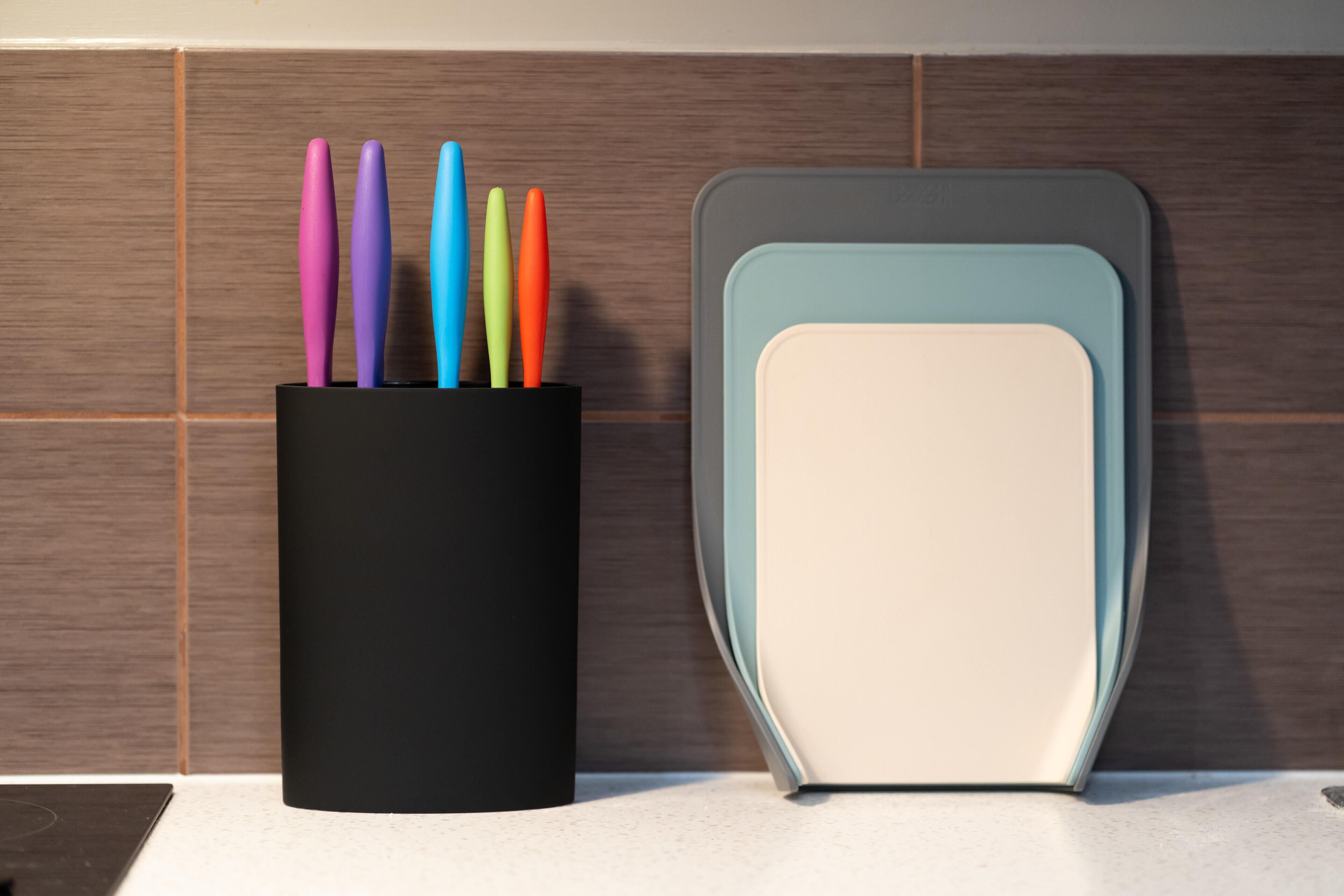 Un porte-ustensiles noir contenant des ustensiles de différentes couleurs, posé sur un plan de travail de cuisine.