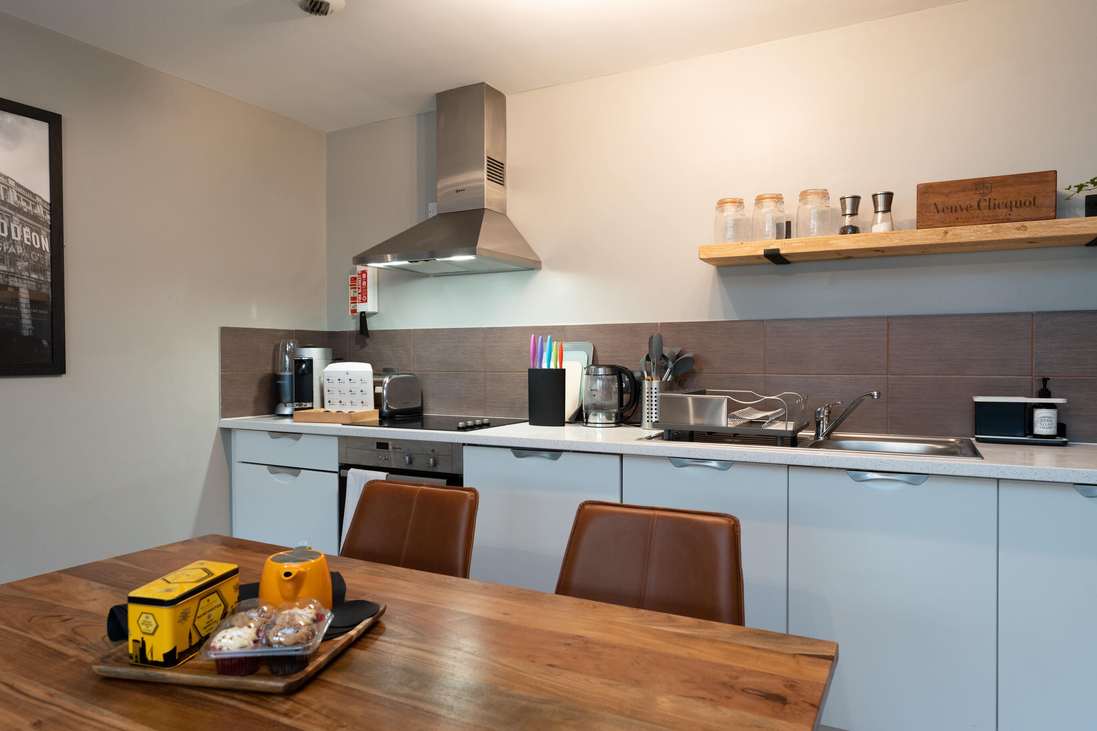 A modern kitchen with a stainless steel range hood, a wooden shelf with kitchen items, a coffee maker, and a toaster.