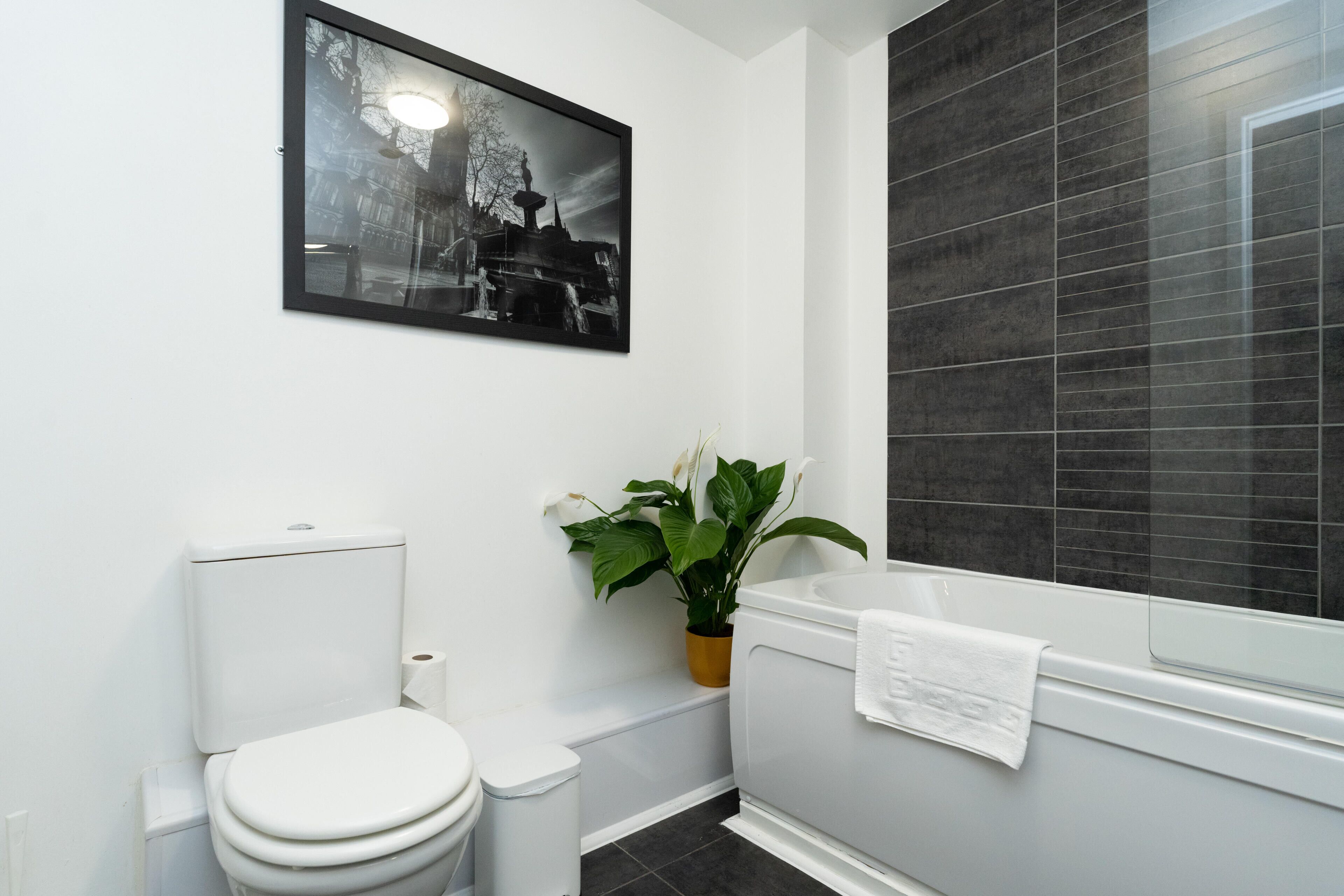 A modern bathroom with a toilet, sink, and bathtub. There is a framed picture on the wall and a potted plant.