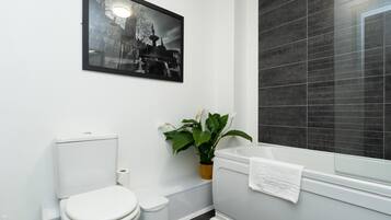 A modern bathroom with a toilet, sink, and bathtub. There is a framed picture on the wall and a potted plant.