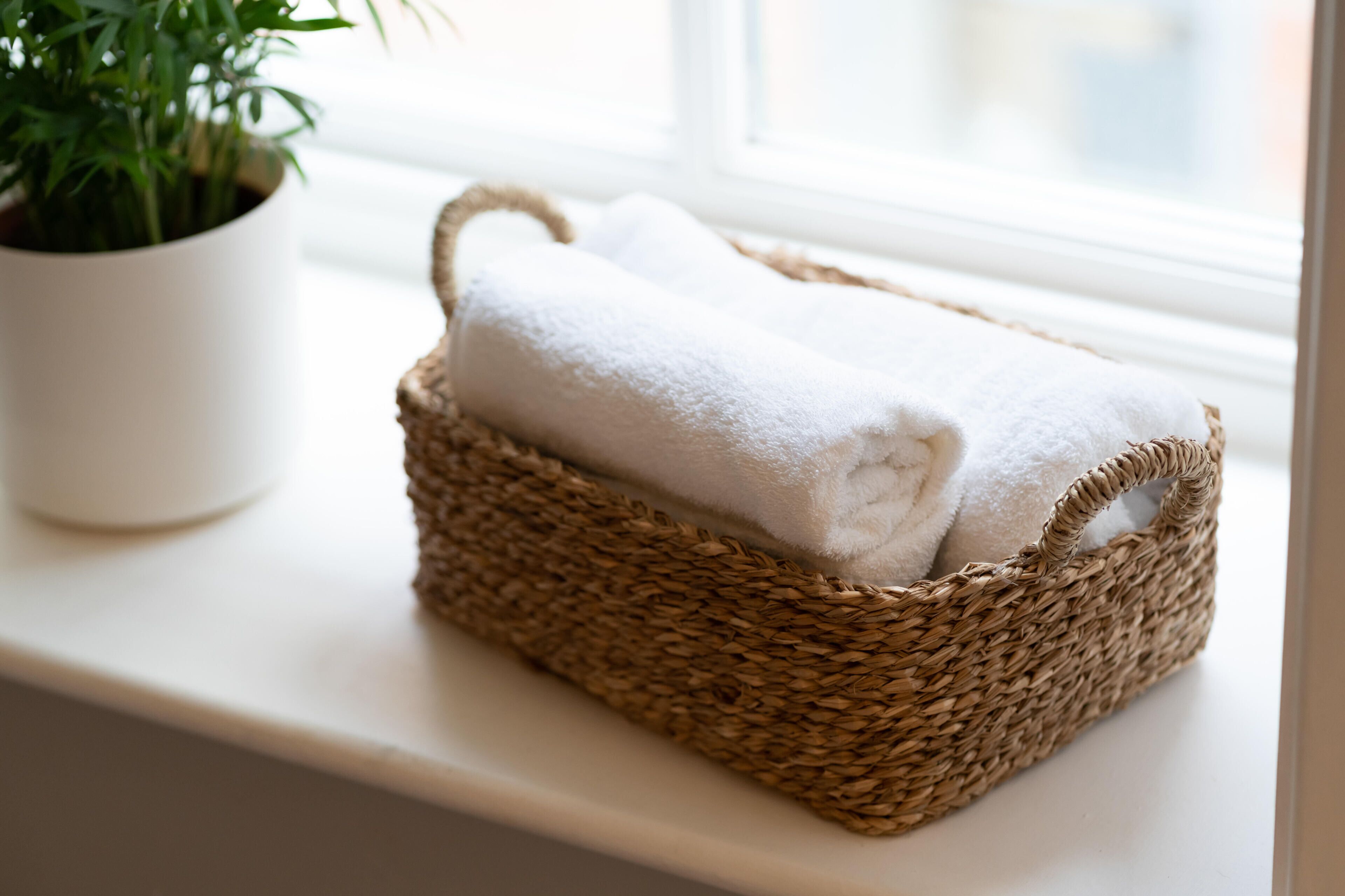 Una cesta tejida con una toalla blanca sobre un alféizar junto a una maceta.