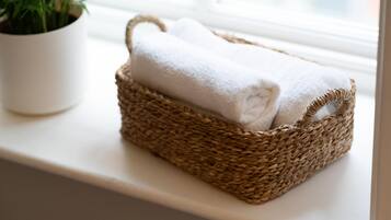 Una cesta tejida con una toalla blanca sobre un alféizar junto a una maceta.