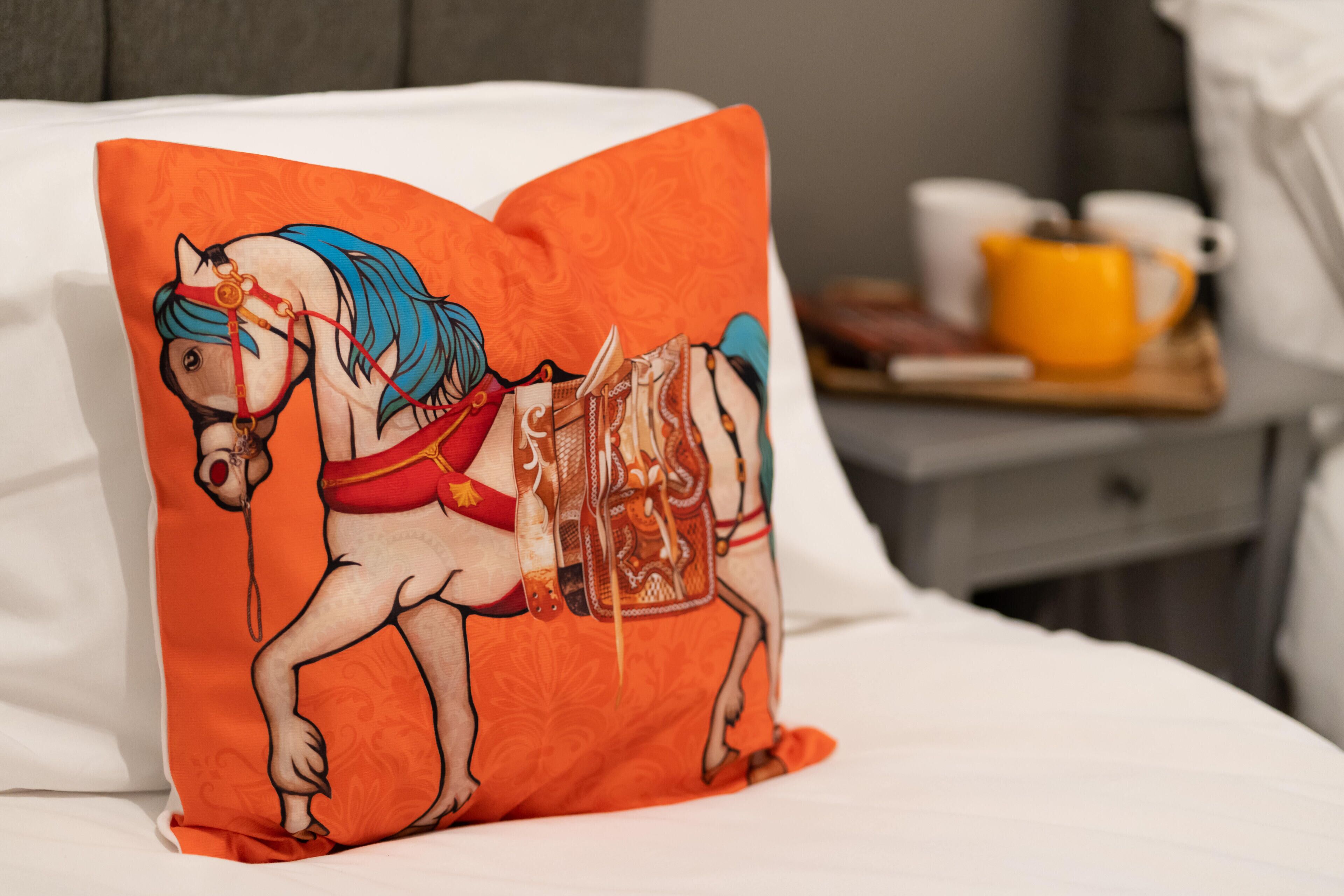 Un coussin orné d’une illustration de cheval, posé sur un lit.