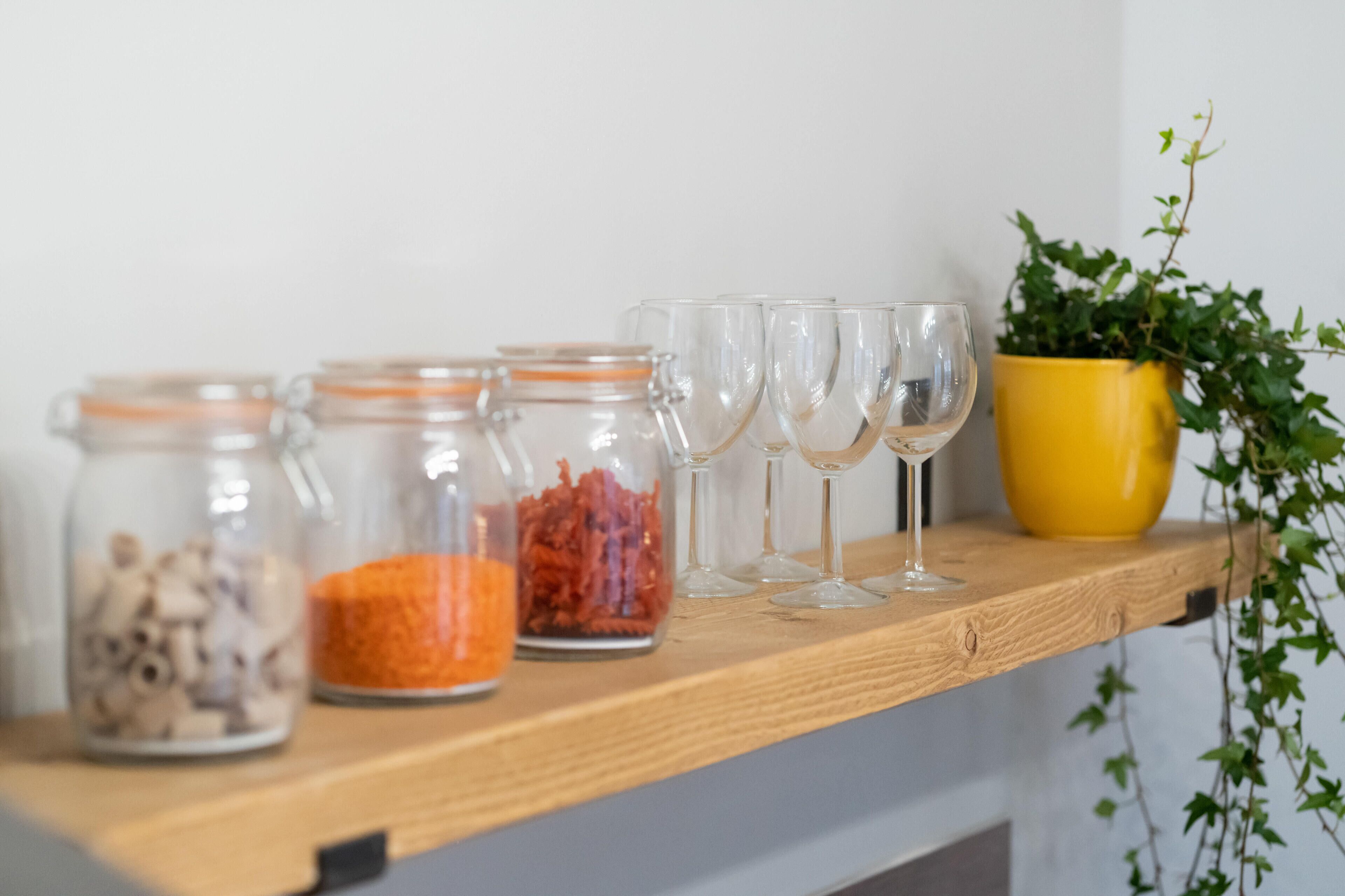 A wooden shelf with glass jars containing various items and empty wine glasses.
